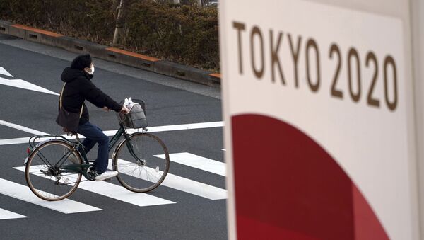 Một người đi xe đạp đeo khẩu trang bảo vệ trên nền biểu ngữ Thế vận hội Tokyo 2020 - Sputnik Việt Nam