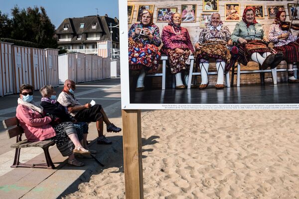 Những người mang khẩu trang trên bãi biển gần bức ảnh trong loạt ảnh Nhân danh mẹ của nhiếp ảnh gia Nadia Ferruha, được trình bày tại Houlgate, tây bắc nước Pháp - Sputnik Việt Nam