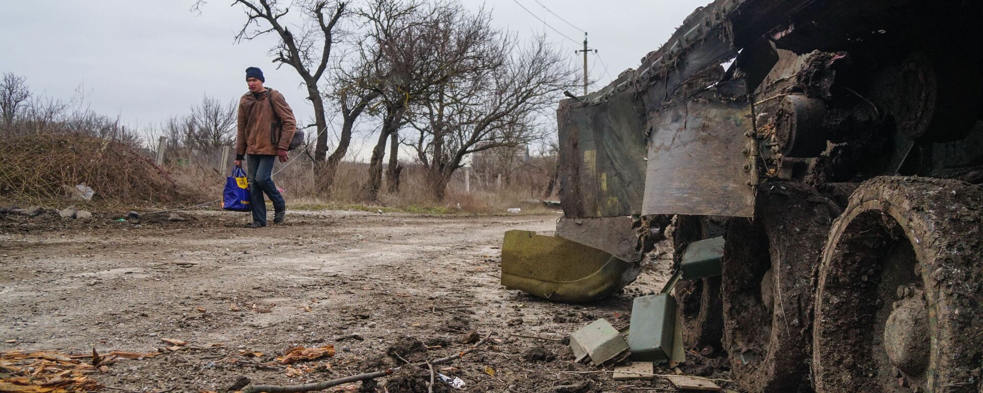 Một cư dân làng Gnutovo đi ngang qua chiếc xe tăng của quân đội Ukraina bị bắn cháy gần Mariupol - Sputnik Việt Nam, 1920, 20.03.2022