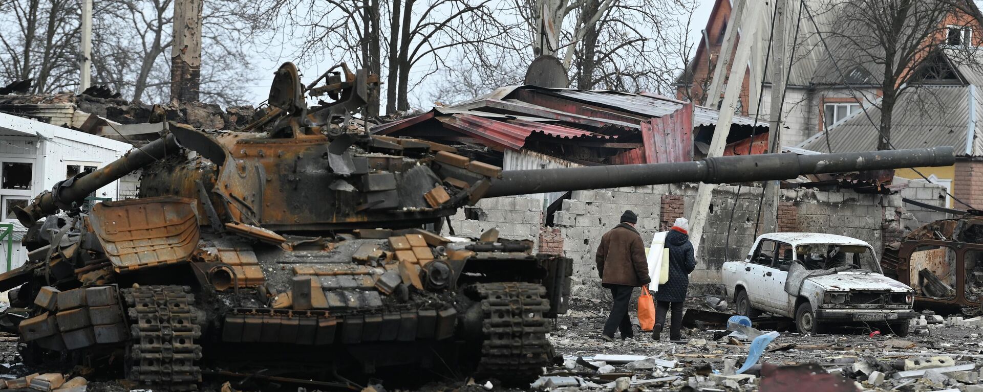 Người dân ở Volnovakha đi bộ về nhà qua một chiếc xe tăng của Lực lượng vũ trang Ukraina bị đắm. - Sputnik Việt Nam, 1920, 25.04.2022