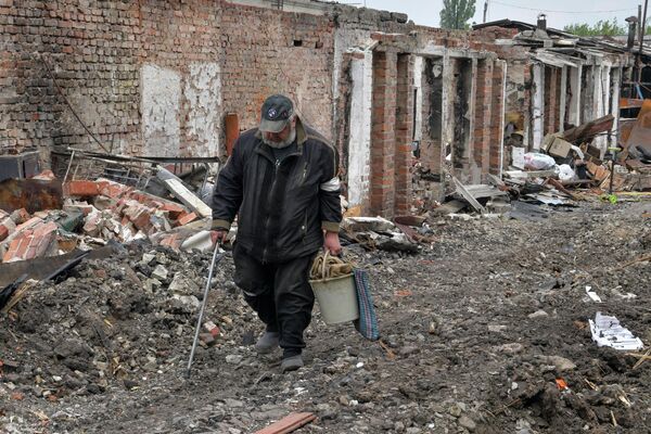 Một người đàn ông đi ngang qua các tòa nhà bị phá hủy trong khu vực tư nhân của thị trấn Popasna - Sputnik Việt Nam