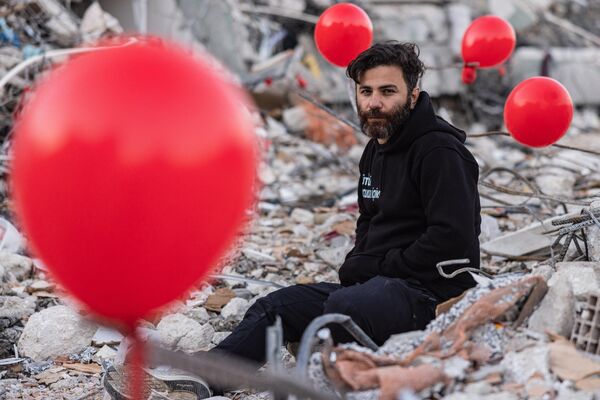 Ogun Sever Okur, 38 tuổi, giữa những quả bóng bay màu đỏ treo trên đống đổ nát những tòa nhà bị sập như biểu tượng &quot;món đồ chơi cuối cùng&quot; của những đứa trẻ chết trong trận động đất ở thành phố Antakya, Thổ Nhĩ Kỳ. - Sputnik Việt Nam