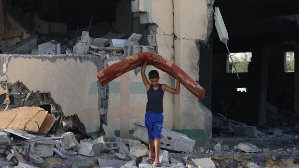 Một cậu bé mang đồ đạc từ một tòa nhà bị phá hủy trong cuộc không kích của Israel ở Khan Yunis, phía nam Dải Gaza - Sputnik Việt Nam