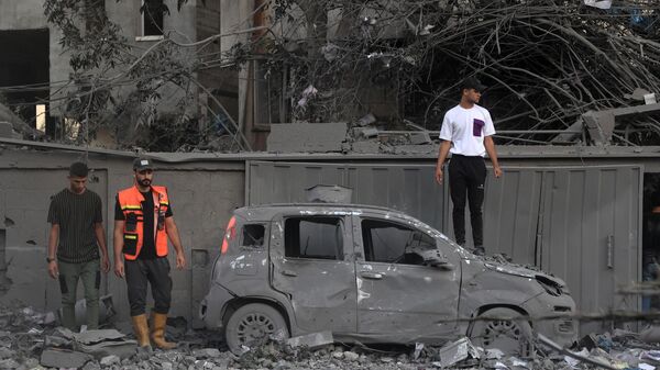 Một nhân viên cứu hộ và người dân đứng bên cạnh một chiếc xe bị cháy sau cuộc tấn công của Israel ở Rafah, phía nam của Dải Gaza - Sputnik Việt Nam