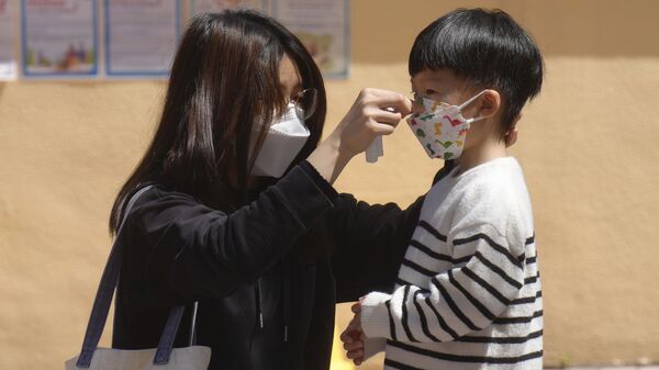 Женщина поправляет маску для лица ребенку в Гонконге, Китай - Sputnik Việt Nam
