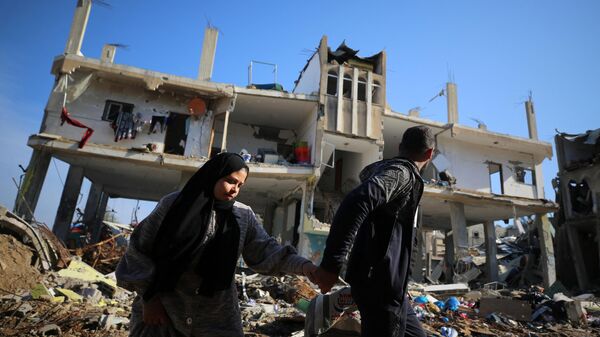 Người Palestine đi ngang qua một tòa nhà bị phá hủy trong trại tị nạn Al-Maghazi ở trung tâm Dải Gaza. - Sputnik Việt Nam