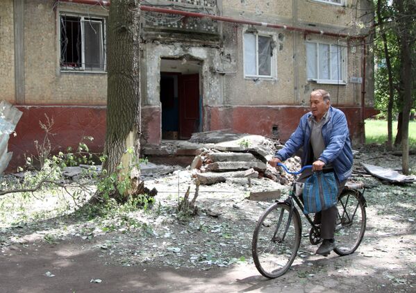Người đàn ông đi xe đạp trong sân chung cư, bị hư hỏng do oanh tạc ở làng Gorlovka tỉnh Donetsk - Sputnik Việt Nam
