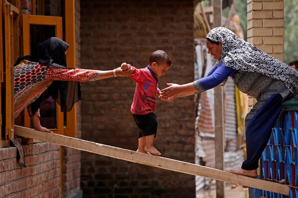 Người phụ nữ giúp trẻ em đi trên tấm ván đến ngôi nhà gần đó trong trận lũ đột ngột, Srinagar - Sputnik Việt Nam