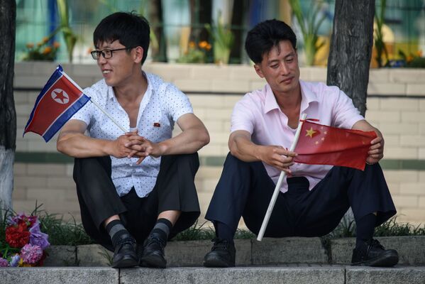Hai người mang cờ Triều Tiên và Trung Quốc ở Quảng trường Kim Nhật Thành, Bình Nhưỡng trong chuyến thăm Triều Tiên của Chủ tịch Trung Quốc Tập Cận Bình   - Sputnik Việt Nam